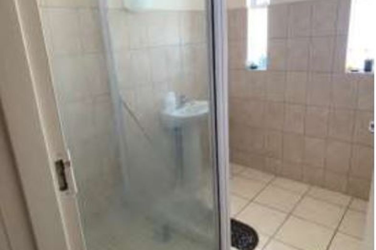 A functional bathroom featuring a pedestal basin, shower enclosure, and neutral wall and floor tiling.
