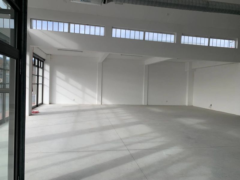 A bright, spacious open-plan retail unit featuring polished concrete floors, high ceilings with exposed ducting, and large clerestory windows providing ample natural light.