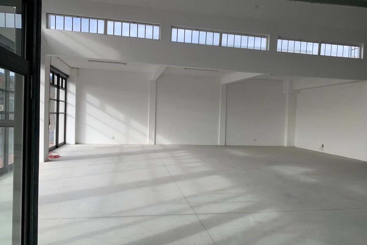 A bright, spacious open-plan retail unit featuring polished concrete floors, high ceilings with exposed ducting, and large clerestory windows providing ample natural light.