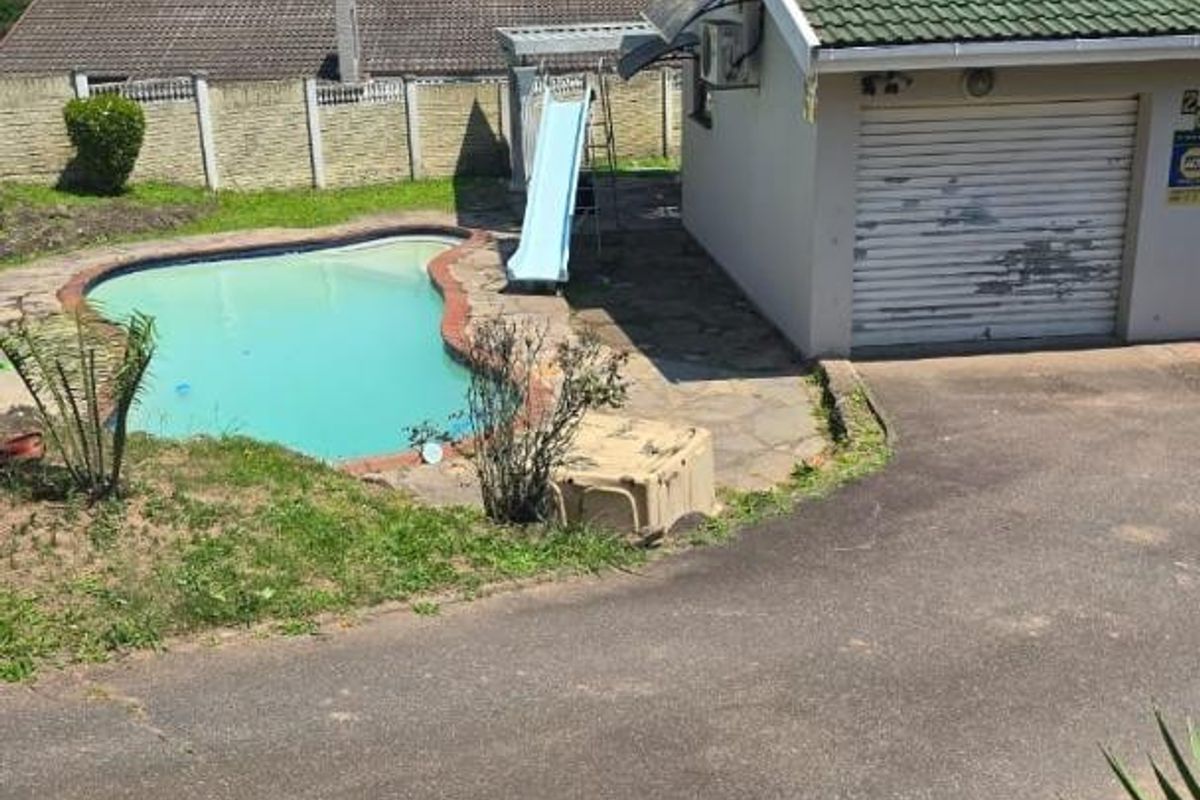 Rear exterior view featuring a swimming pool, paved driveway, and a single garage with a tiled roof.