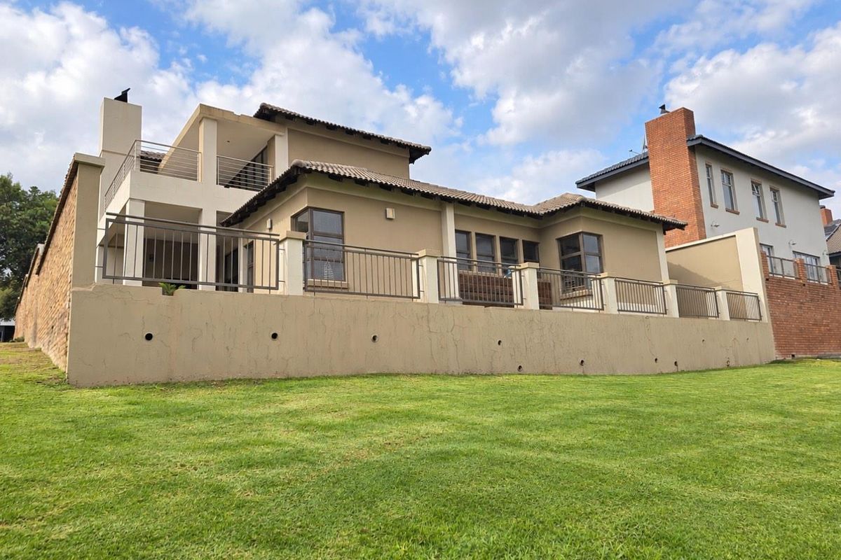Rear elevation of a multi-story house featuring a large lawn, raised patio with metal railings, and a tiled roof.