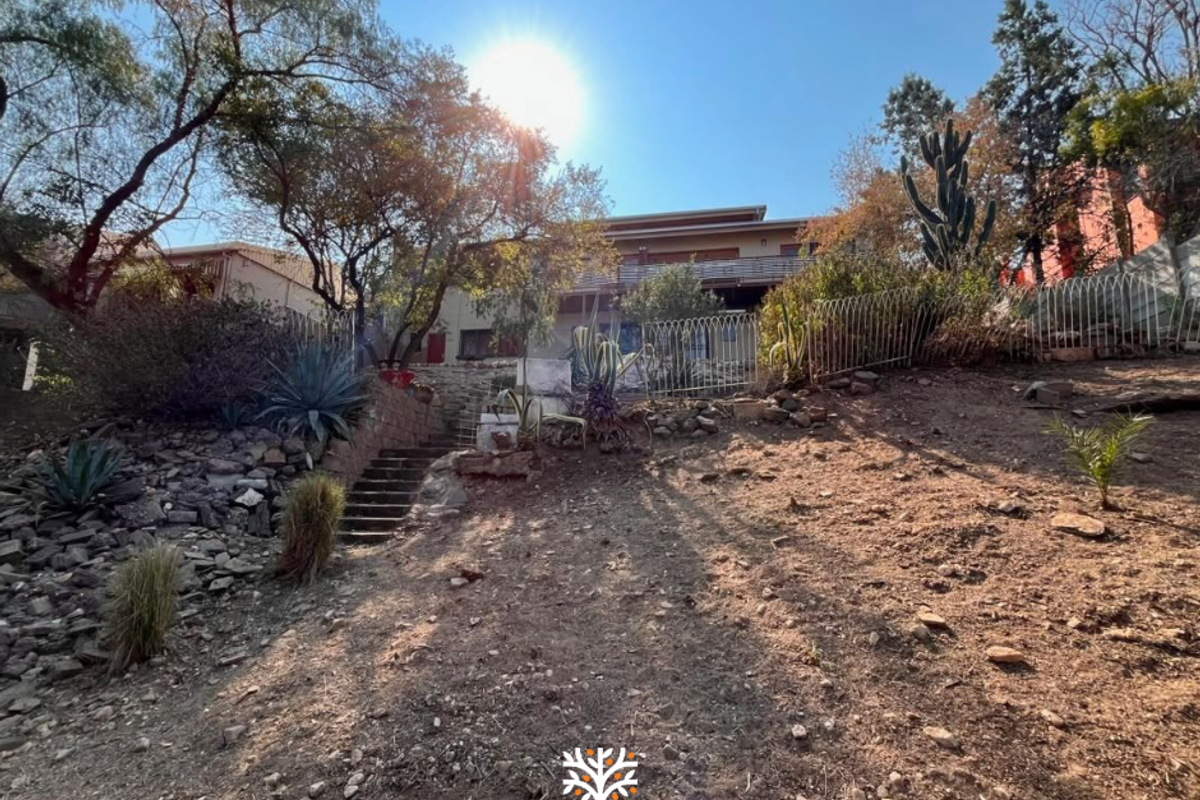 Rear view of the property featuring a sloped garden, stone retaining walls, concrete stairs, and an elevated balcony.