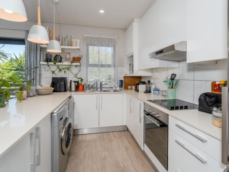 Modern kitchen featuring white cabinetry, stone countertops, integrated appliances, and a tiled backsplash, with direct access to an outdoor balcony area.