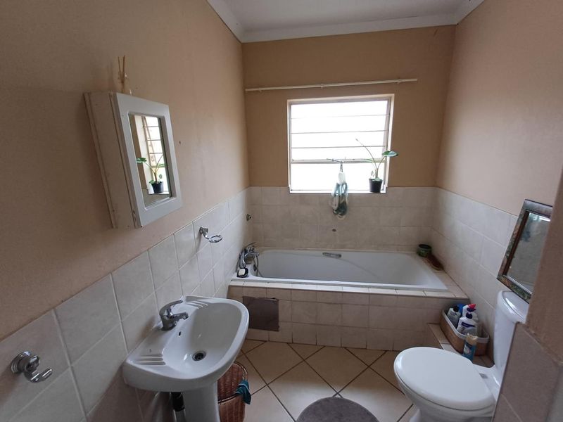 A functional bathroom featuring a built-in bathtub, pedestal basin, and toilet, with neutral wall and floor tiling.
