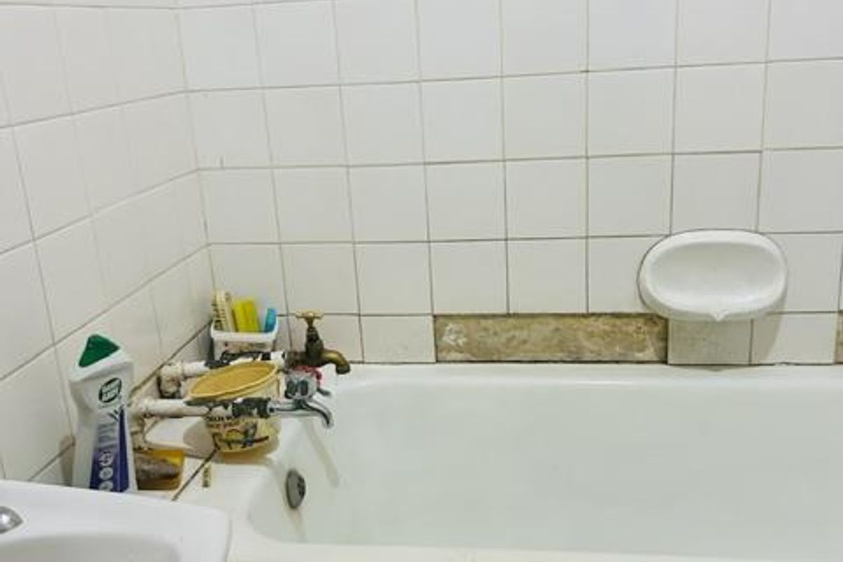 A bathroom featuring a bathtub with exposed plumbing and damaged wall and apron tiling, requiring maintenance and cosmetic repairs.