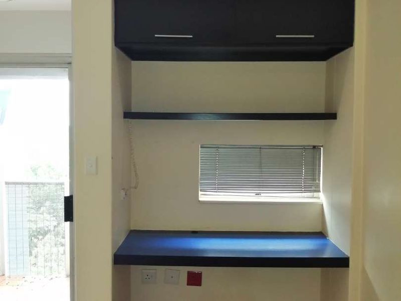 A dedicated home office space featuring a built-in desk, overhead storage cabinetry, fixed shelving, and direct access to a balcony through a sliding glass door.
