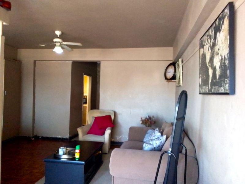 A living room featuring parquet flooring and a ceiling fan, requiring cosmetic updates to the wall finishes and general maintenance.