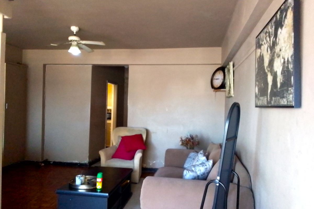 A living room featuring parquet flooring and a ceiling fan, requiring cosmetic updates to the wall finishes and general maintenance.