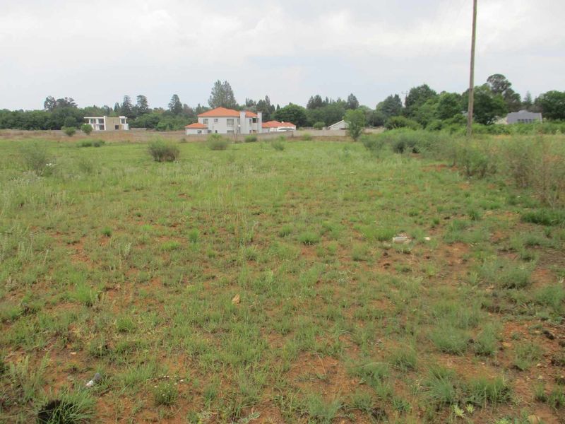 A view of a vacant residential plot of land with natural grass cover and a utility pole, situated in a developed residential area.