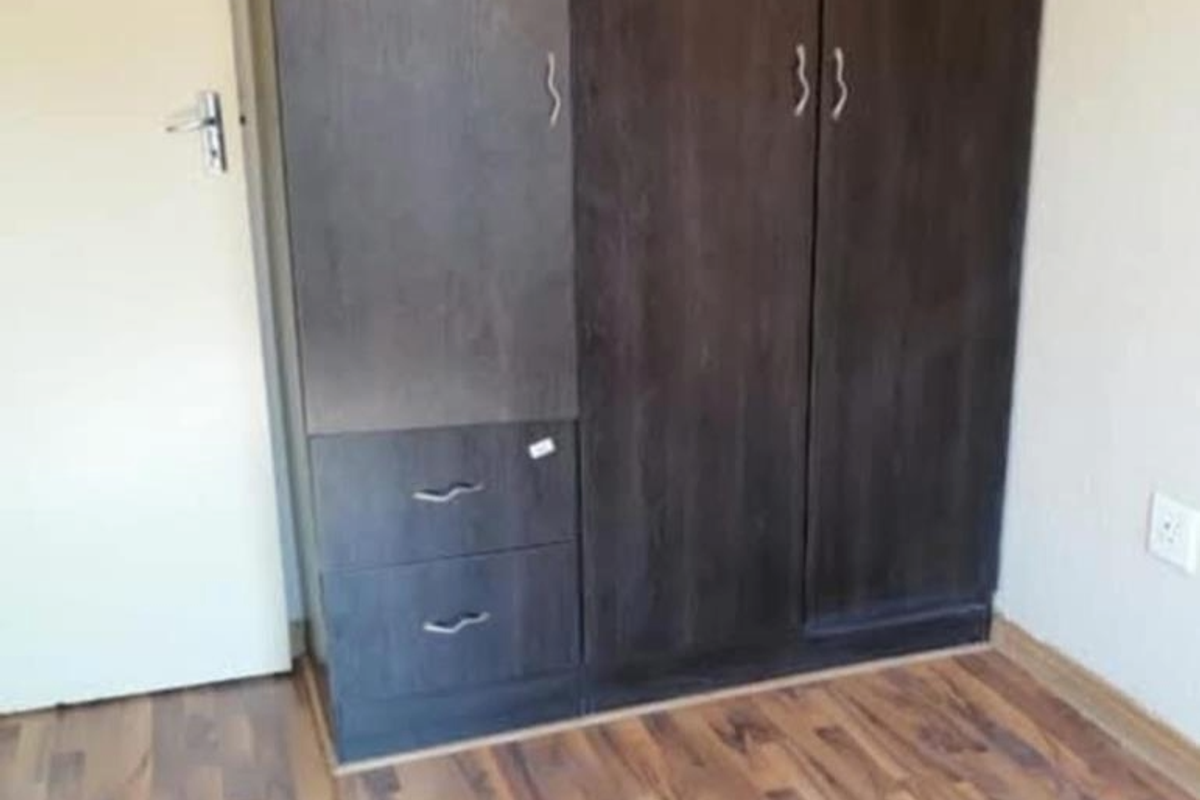 A bedroom featuring dark wood-finish built-in wardrobes and laminate flooring.
