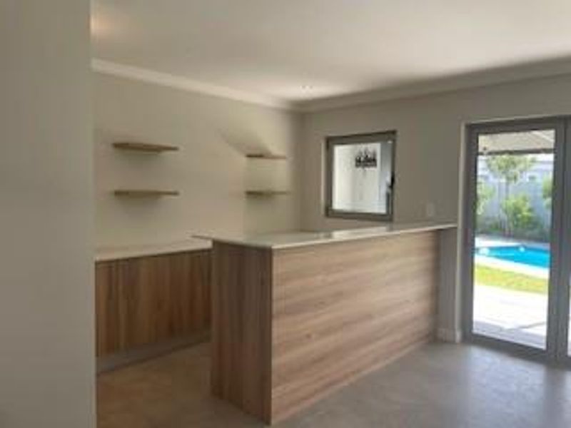 A modern, empty bar area featuring wood-finish cabinetry, a built-in counter, floating shelves, and direct access to the outdoor pool area through a sliding door.