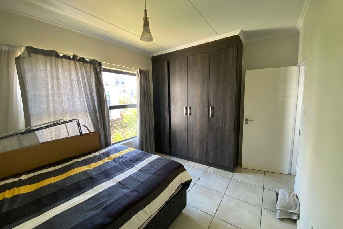 A bedroom featuring built-in dark wood cabinetry, tiled flooring, and a window providing natural light.