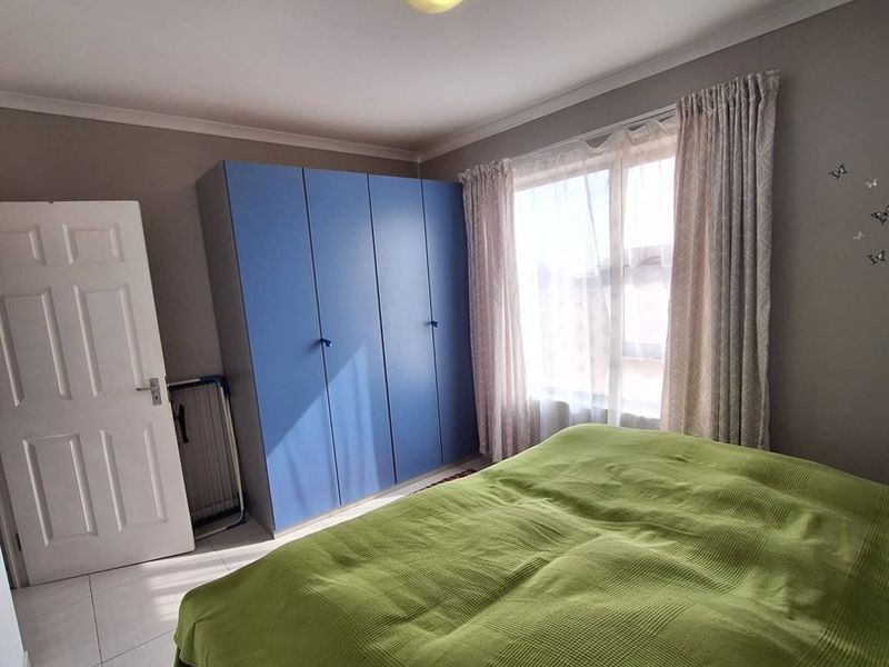 A functional bedroom featuring built-in blue cupboards, tiled flooring, and natural light from the window.
