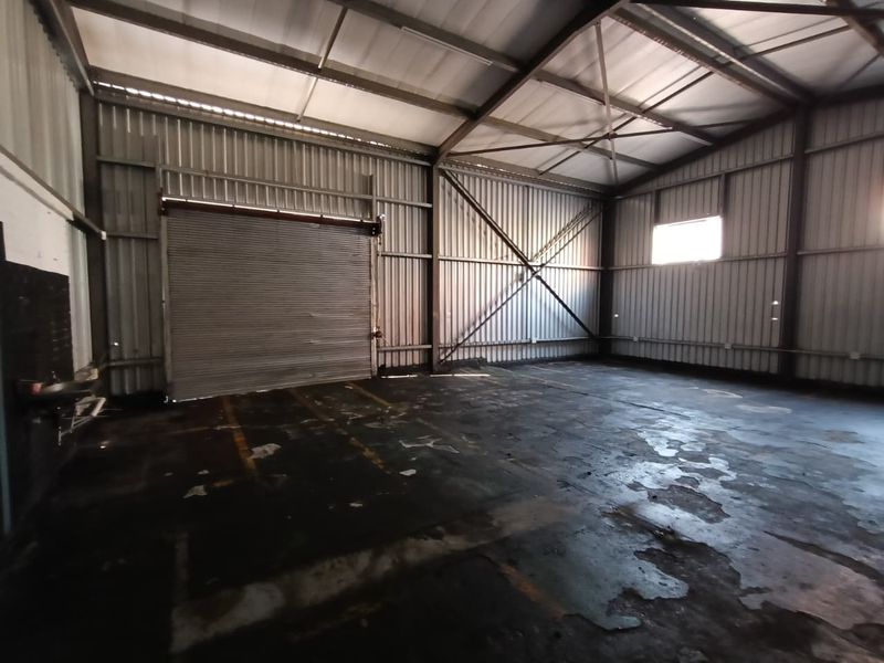 Spacious industrial utility area featuring a high-clearance steel frame structure, corrugated metal walls, and a large roller shutter door for vehicle or equipment access.