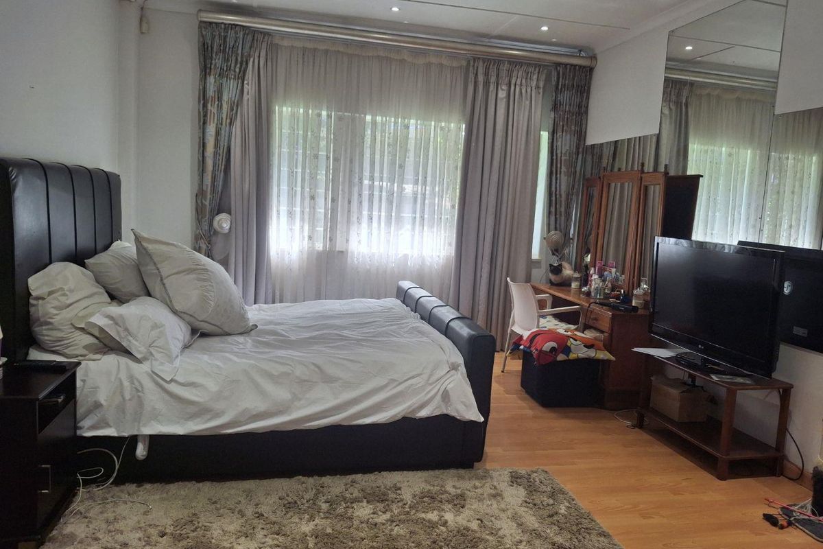 A spacious bedroom featuring laminate flooring, recessed ceiling lighting, and a large wall-mounted mirror, offering a comfortable and functional living space.