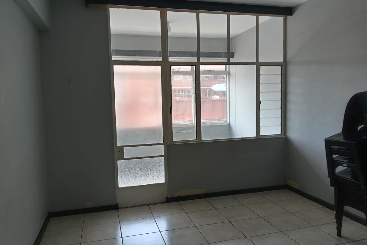 A bright, empty living room featuring tiled flooring and a large glass partition wall with an integrated door leading to an adjacent space.