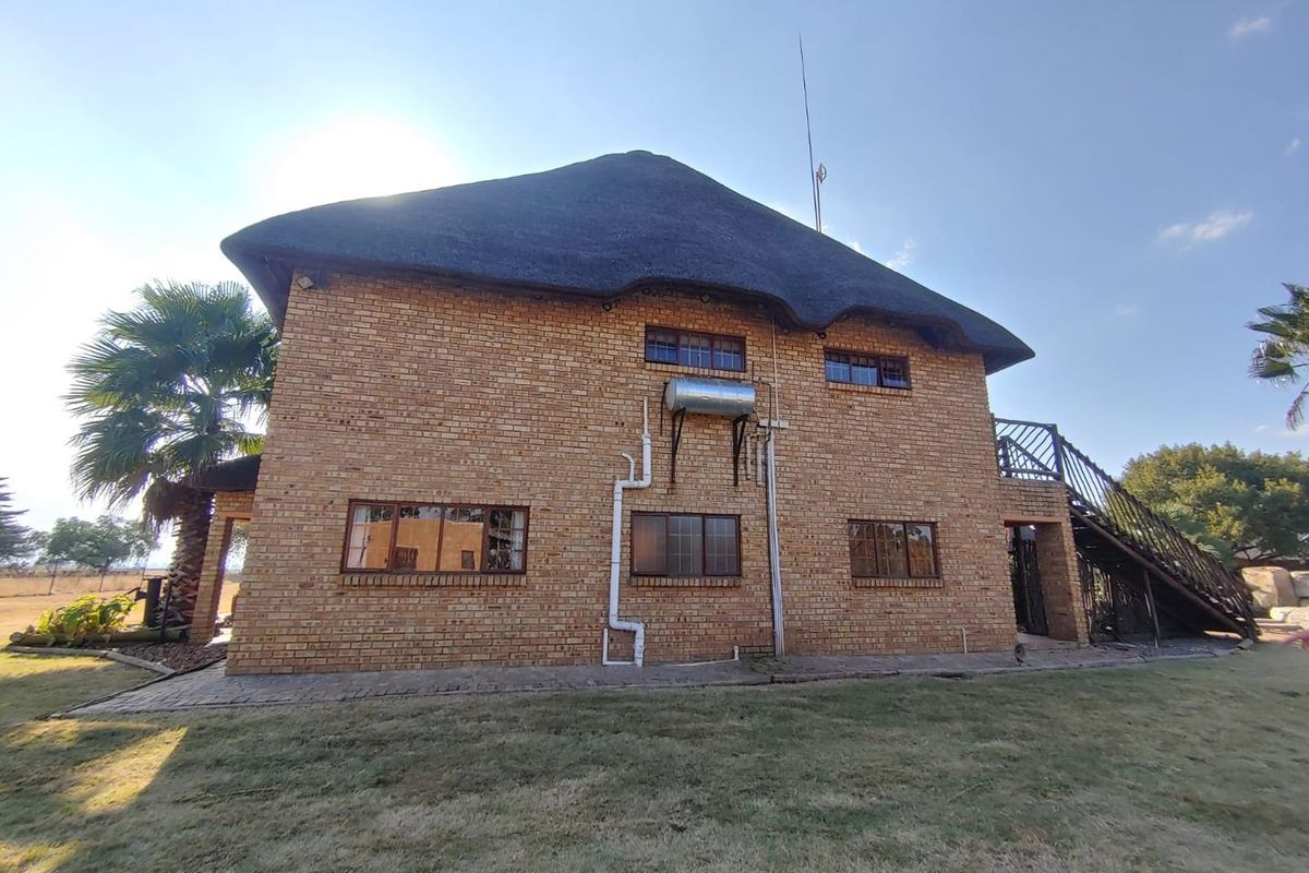 A side view of a double-story face-brick dwelling featuring a traditional thatched roof, external staircase, and solar geyser installation.