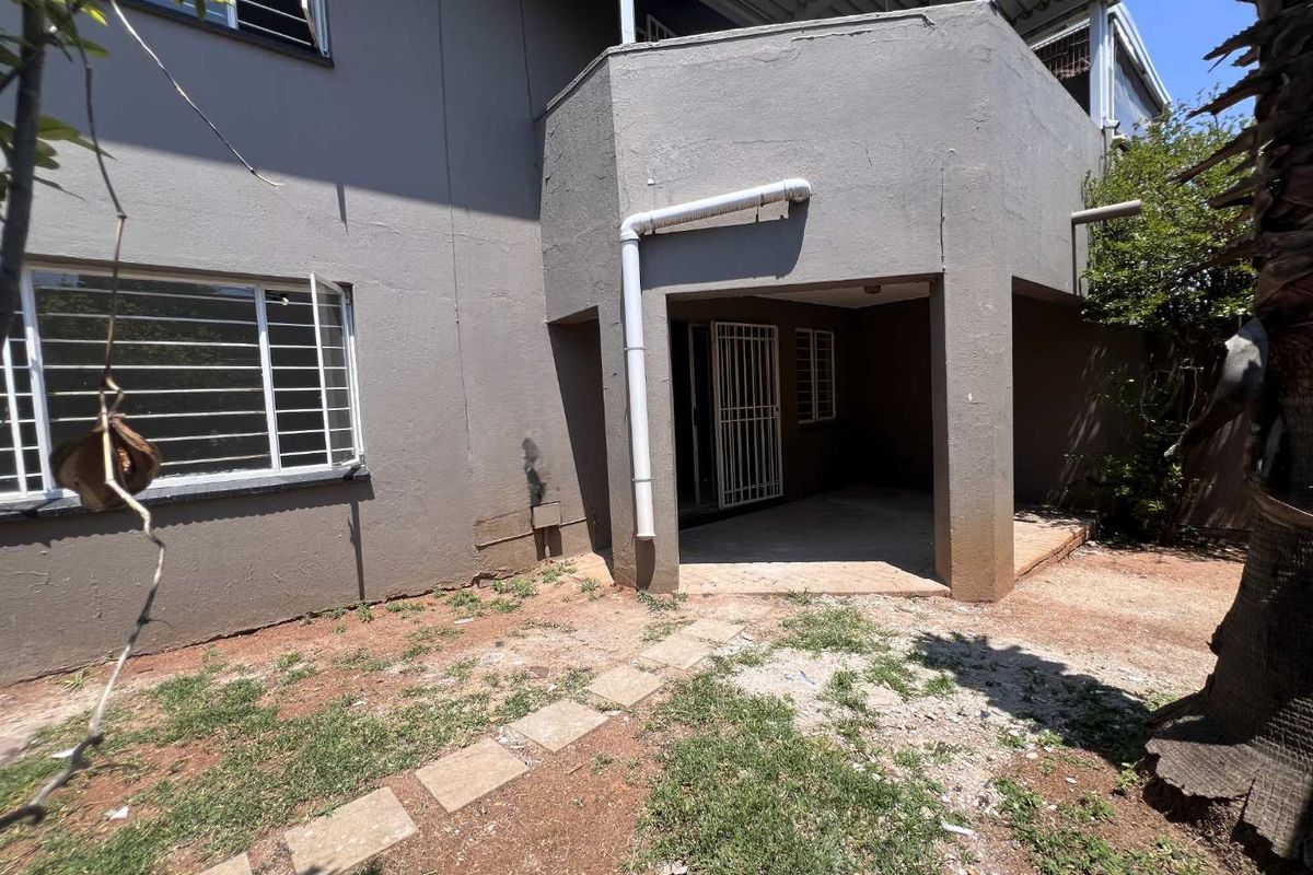 Rear view of the apartment building featuring a covered patio area, security bars on windows, and an unlandscaped garden space.