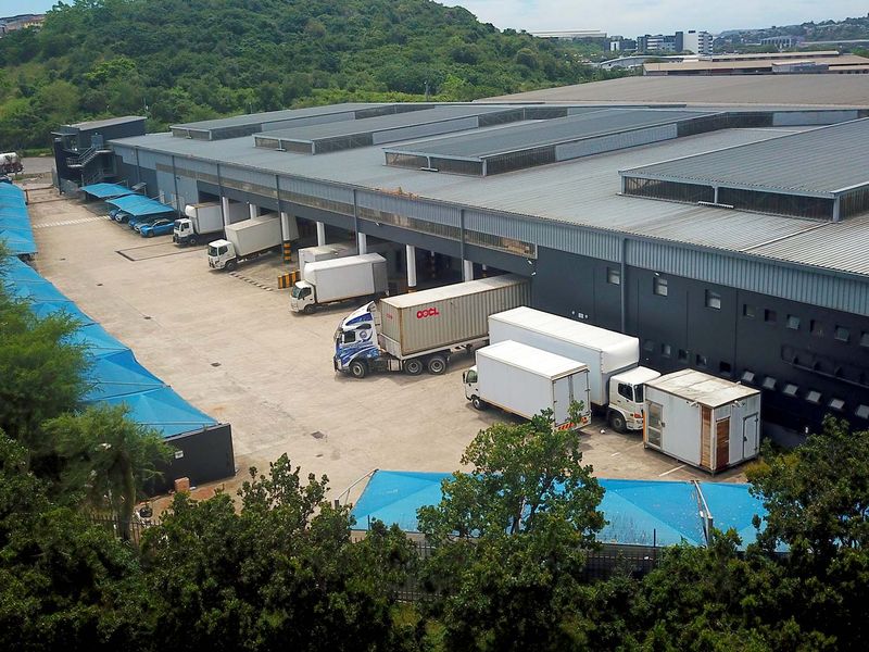 Aerial view of an industrial warehouse facility featuring a large concrete loading yard, multiple loading bays, and covered parking areas.