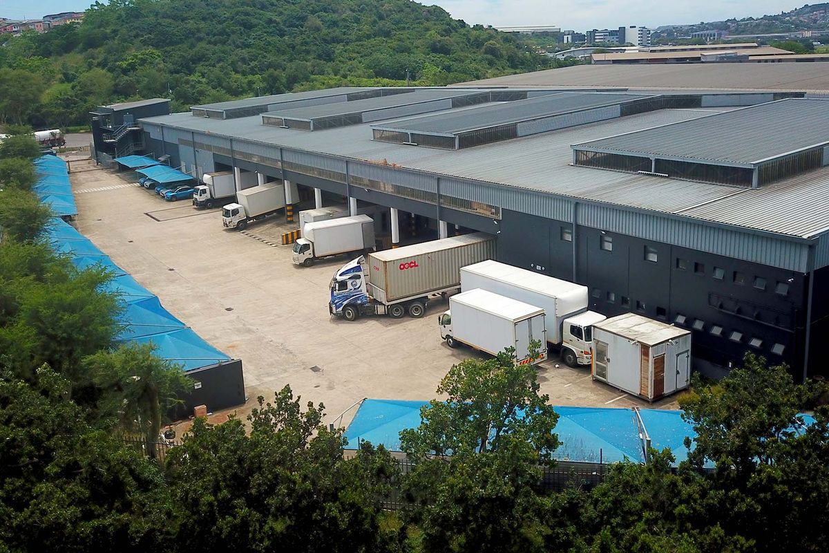 Aerial view of an industrial warehouse facility featuring a large concrete loading yard, multiple loading bays, and covered parking areas.
