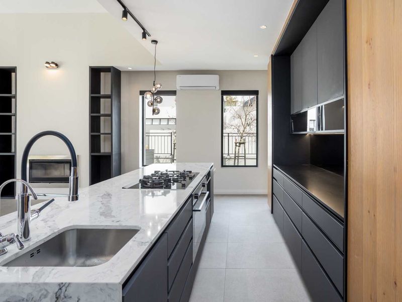Modern kitchen featuring a marble island with integrated gas cooktop, sleek dark cabinetry, built-in oven, and high-end finishes in an open-plan living space.