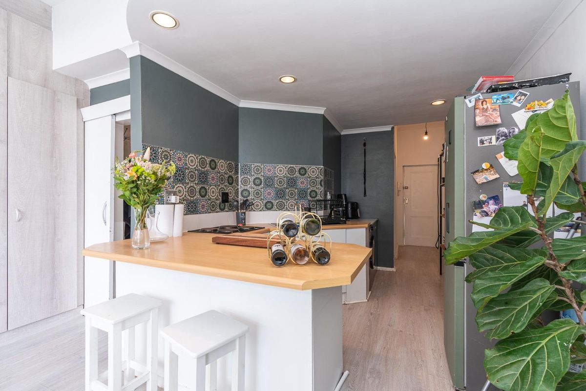 A functional kitchen featuring a breakfast bar, patterned tile backsplash, recessed lighting, and light wood-look flooring in an open-plan layout.