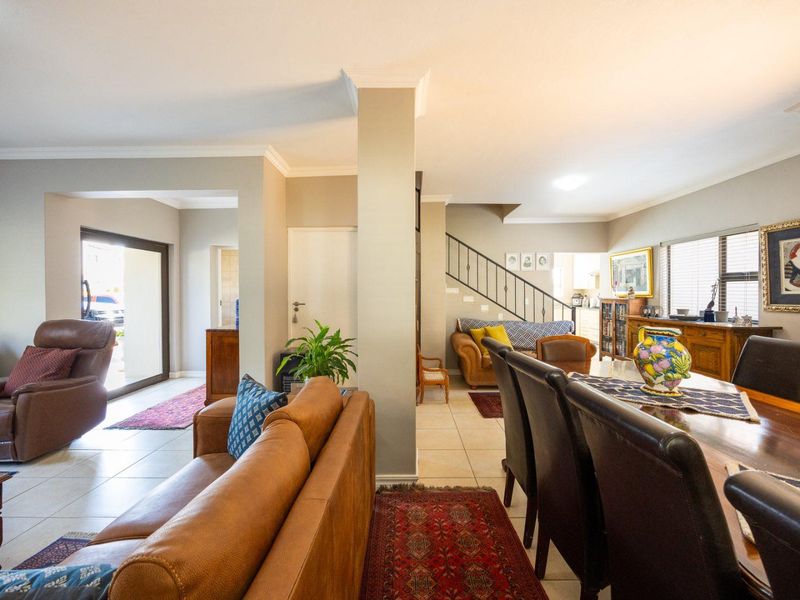 Spacious open-plan living and dining area featuring tiled flooring, a central structural pillar, and a staircase with a metal railing.