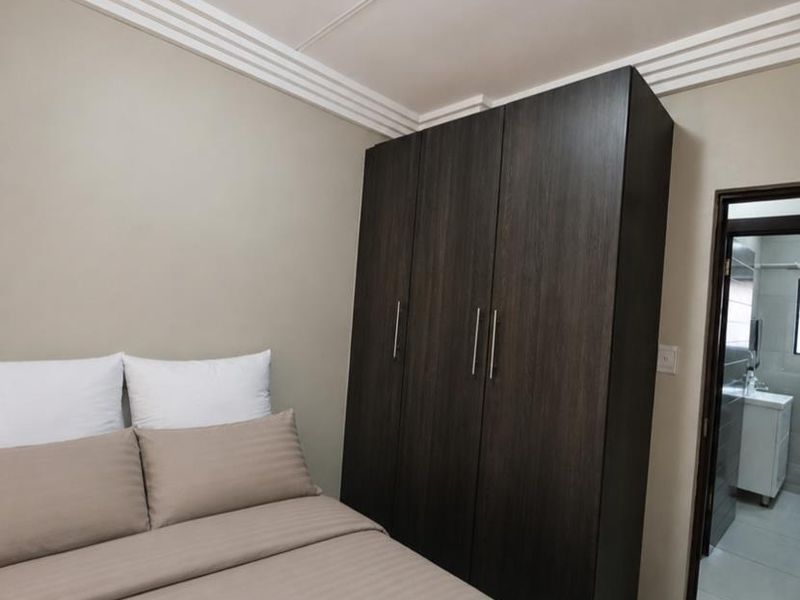 A well-maintained bedroom featuring a dark wood built-in wardrobe, decorative ceiling cornices, and neutral tiled flooring with an adjoining en-suite bathroom.