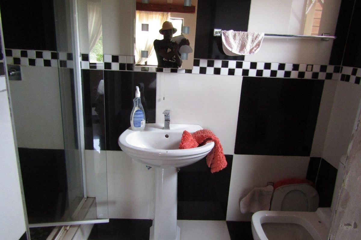A compact bathroom featuring a pedestal sink, shower enclosure, and toilet with a high-contrast black and white checkered tile design.