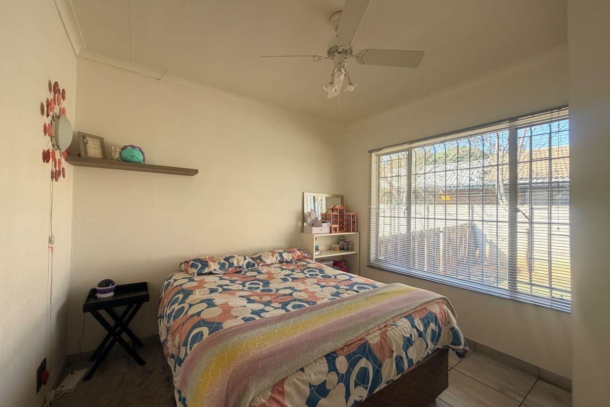 A functional bedroom featuring tiled flooring, a ceiling fan, and large windows fitted with security bars for added peace of mind.