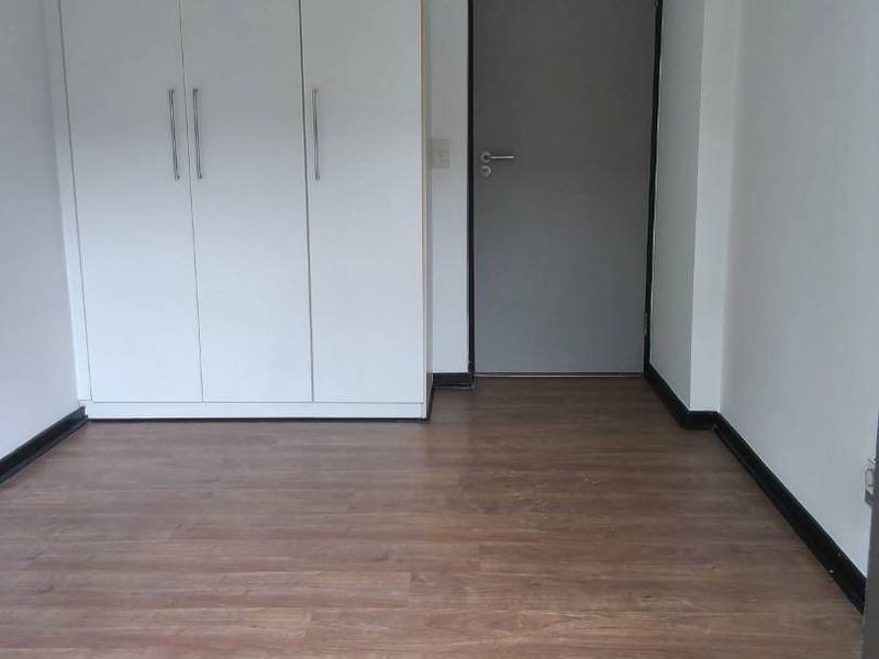 A clean, empty bedroom featuring modern laminate flooring and a built-in white wardrobe, providing a neutral canvas for personalization.
