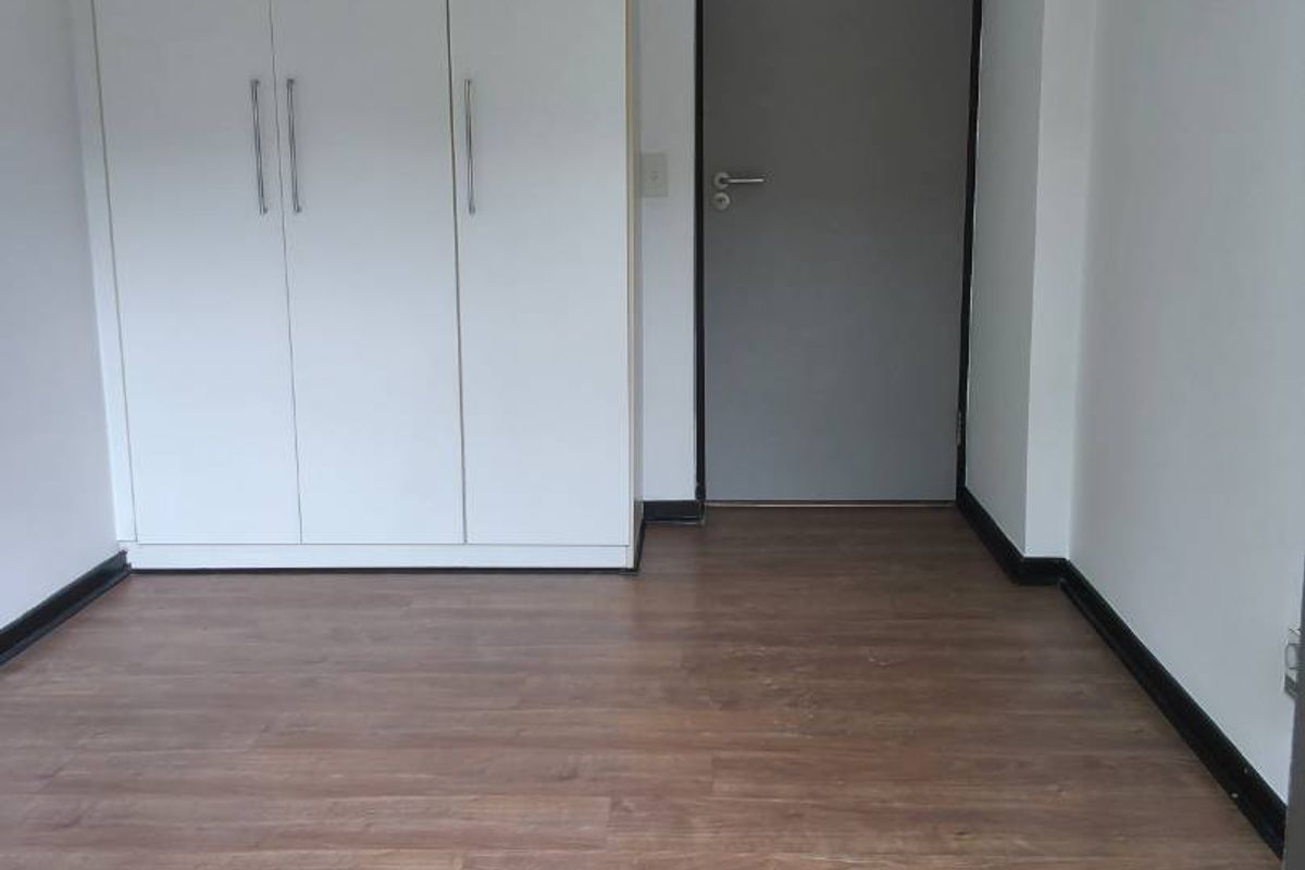 A clean, empty bedroom featuring modern laminate flooring and a built-in white wardrobe, providing a neutral canvas for personalization.