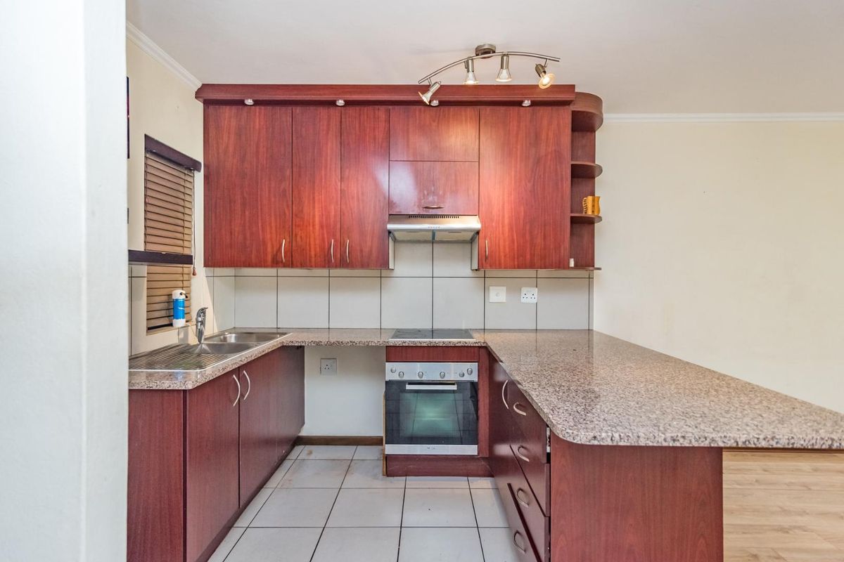 A functional kitchen featuring dark wood cabinetry, granite countertops, a built-in oven, hob, extractor fan, and a stainless steel sink.