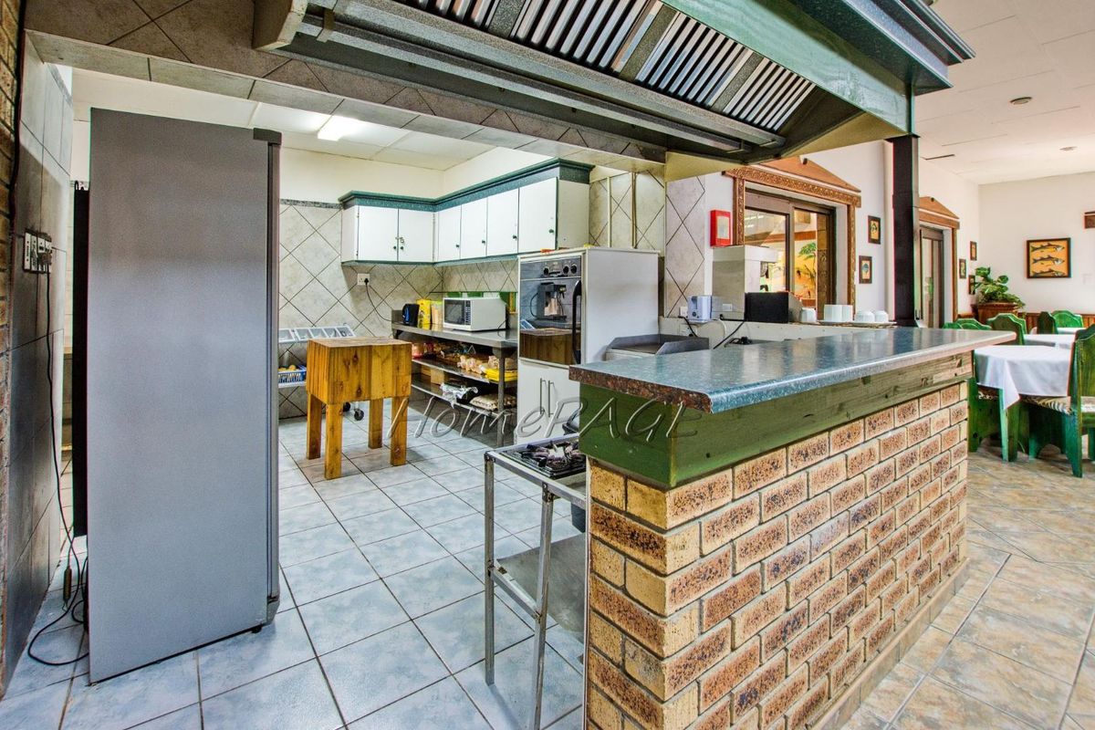 A functional commercial-style kitchen featuring a brick breakfast bar, tiled flooring, built-in cabinetry, and an overhead extractor hood.