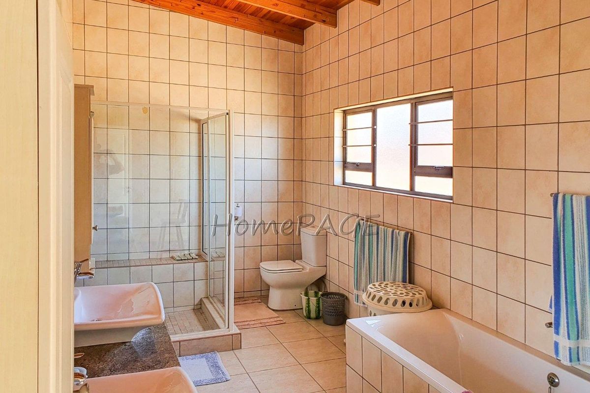 A functional bathroom featuring a glass-enclosed shower, a bathtub, dual vanity basins, and a high-pitched timber ceiling.