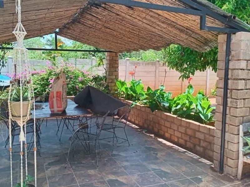 Covered outdoor patio area featuring a thatched roof, brick support pillars, tiled flooring, and a built-in brick planter box.