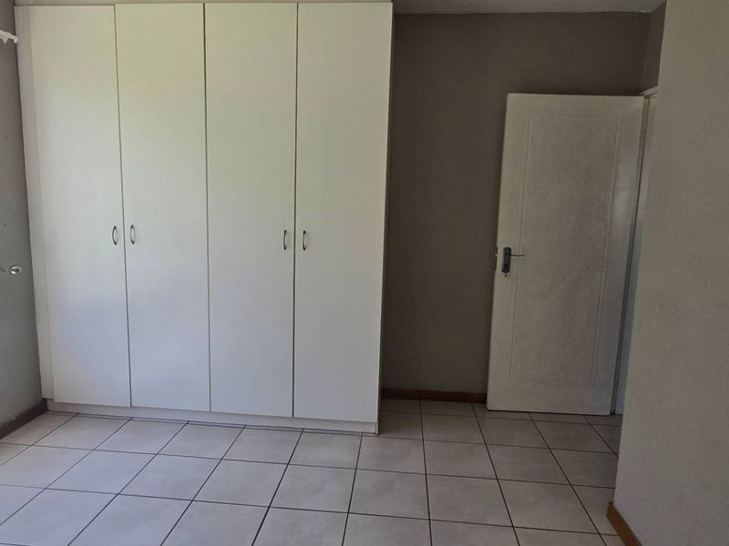 A bright, empty bedroom featuring tiled flooring, built-in cupboards, and large windows with security bars, offering a clean canvas for personalization.