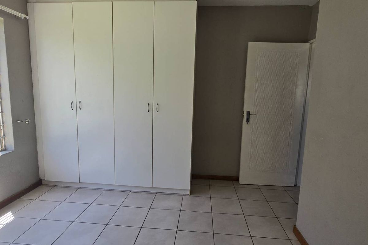 A bright, empty bedroom featuring tiled flooring, built-in cupboards, and large windows with security bars, offering a clean canvas for personalization.