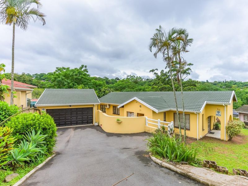 Front view of a yellow single-story house featuring a tiled roof, attached garage, and paved driveway set within a landscaped garden.