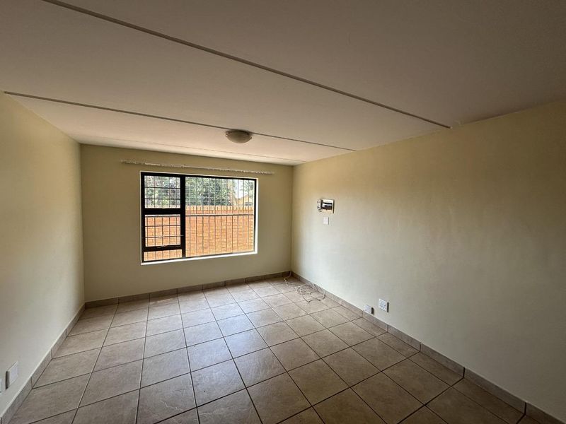 An empty living room featuring tiled flooring, a window with security bars, and neutral wall paint, offering a blank canvas for personalization.