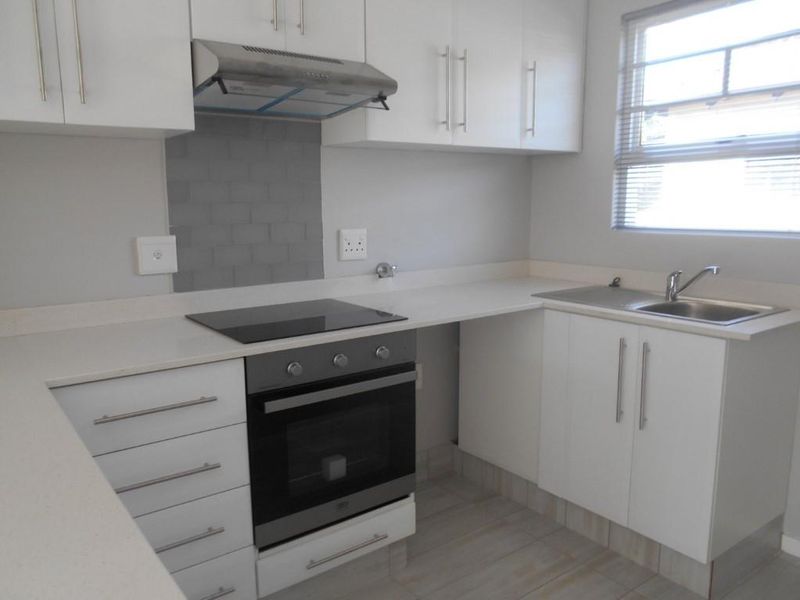 A clean, modern kitchen featuring white cabinetry, stone countertops, a built-in oven with electric hob, and a stainless steel sink.