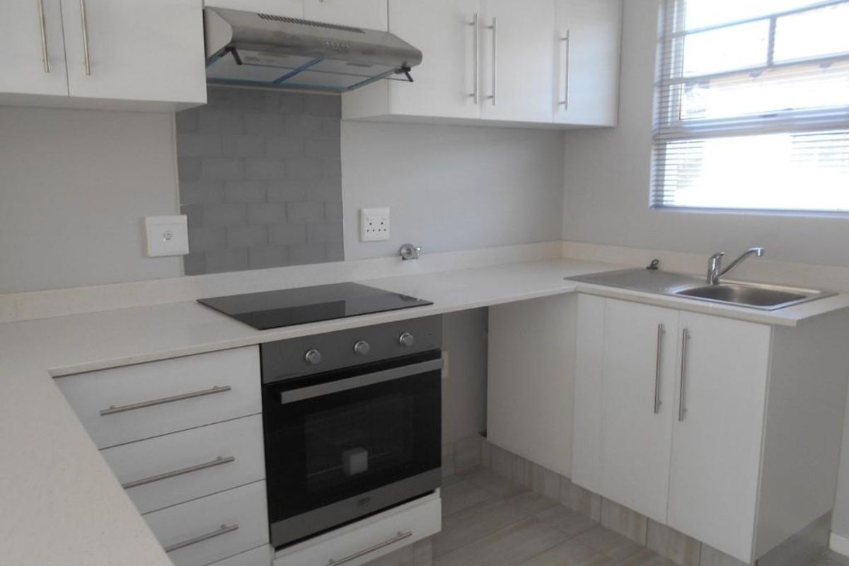 A clean, modern kitchen featuring white cabinetry, stone countertops, a built-in oven with electric hob, and a stainless steel sink.