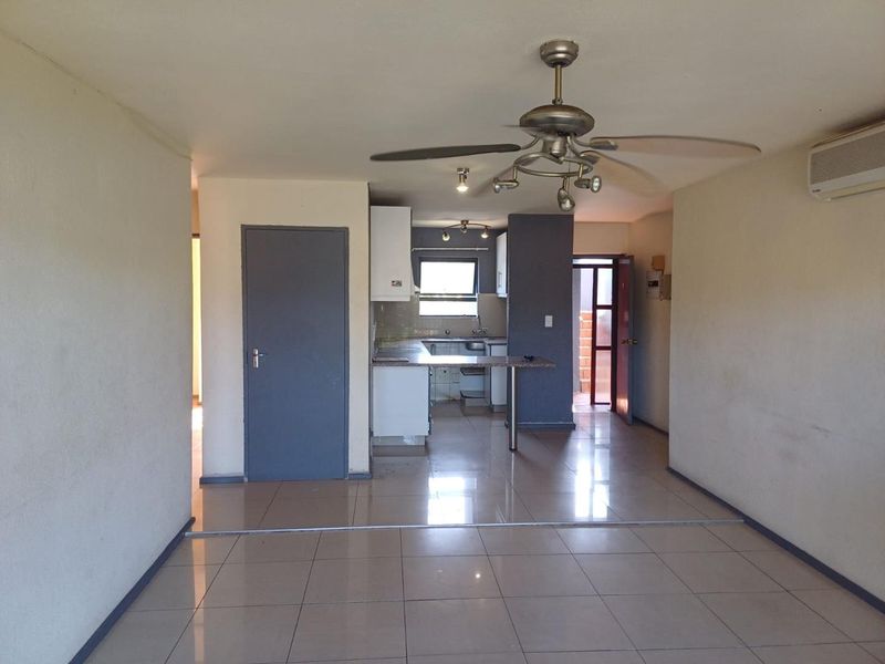 An open-plan living and kitchen area featuring tiled flooring, a ceiling fan, air conditioning, and functional kitchen cabinetry.