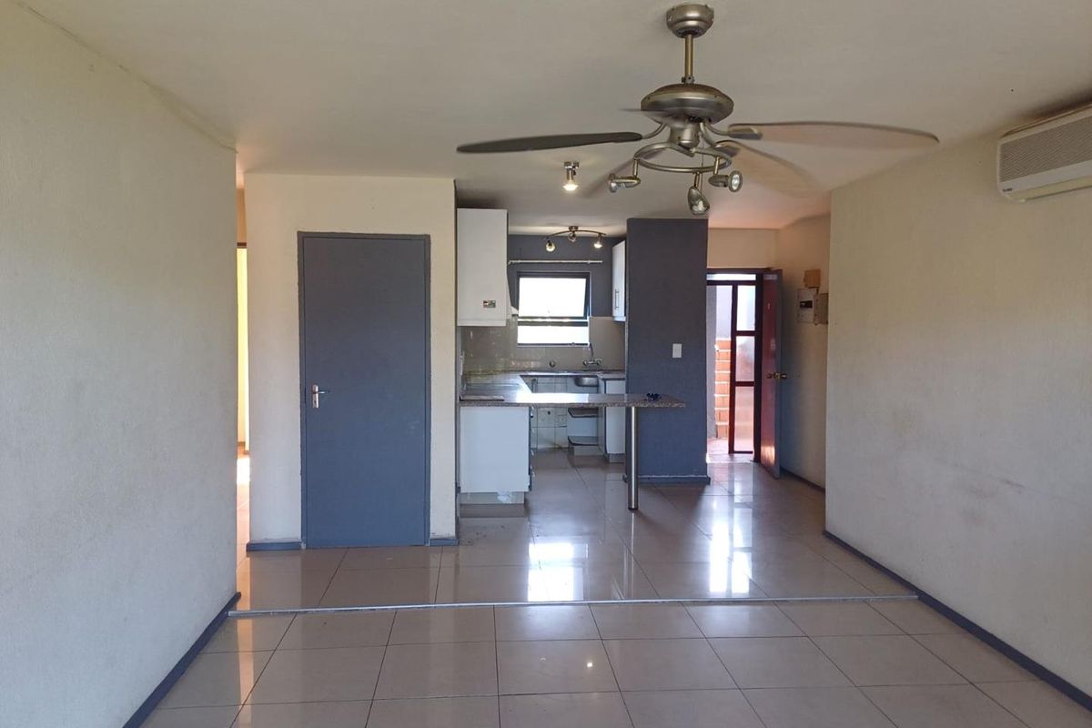 An open-plan living and kitchen area featuring tiled flooring, a ceiling fan, air conditioning, and functional kitchen cabinetry.