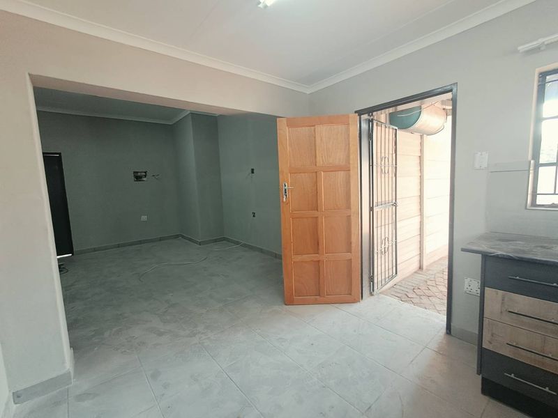 An open-plan living area featuring tiled flooring, coved cornicing, and direct access to an outdoor space through a timber door and security gate.