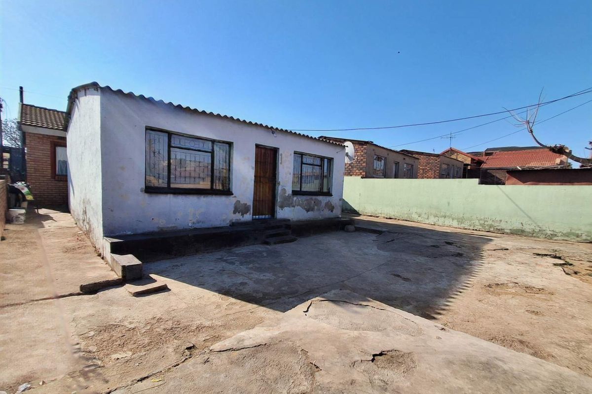 Rear exterior view of the property featuring a concrete patio area, perimeter wall, and a structure with security bars on the windows.