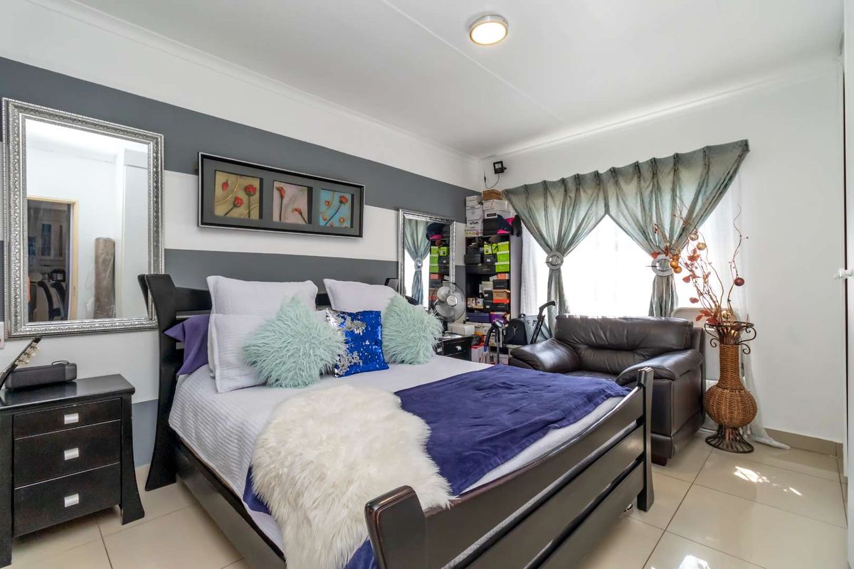 A well-lit bedroom featuring neutral tiled flooring, crisp white ceiling cornices, and a feature wall with horizontal striped paint.