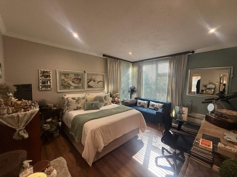 A well-lit bedroom featuring laminate flooring, recessed downlighting, and large windows with venetian blinds, offering a comfortable and functional living space.