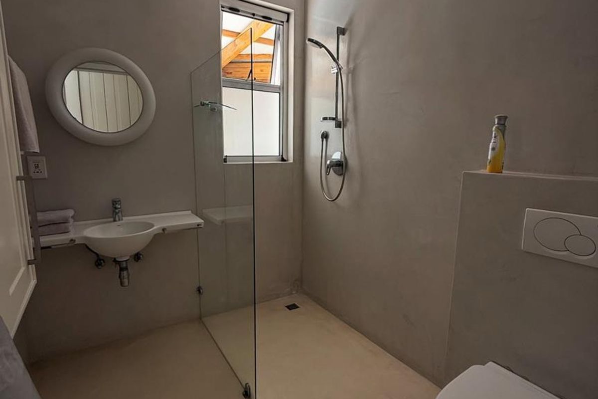 Modern bathroom featuring a walk-in glass shower, wall-mounted basin, and concealed cistern toilet with polished concrete-style finishes.