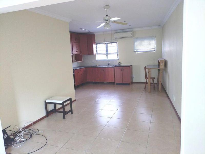 Open-plan kitchen and living area featuring tiled flooring, built-in wooden cabinetry, and a ceiling fan, offering a functional and versatile living space.